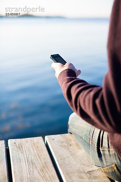 Mann auf einer Mole mit einem Mobiltelefon  Schweden.