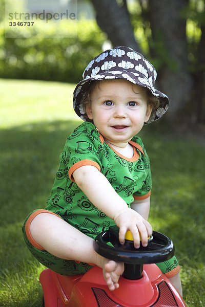 Kleiner Junge spielen mit einem Spielzeugauto in einem Garten  Schweden.