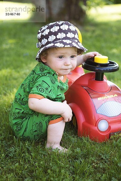 Kleiner Junge spielen mit einem Spielzeugauto in einem Garten  Schweden.