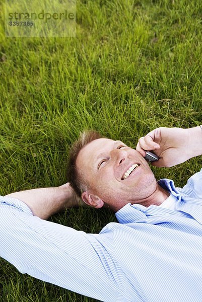 Mann liegt im Gras und redet auf dem Handy.