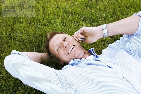 Mann im Gras liegend mit Handy