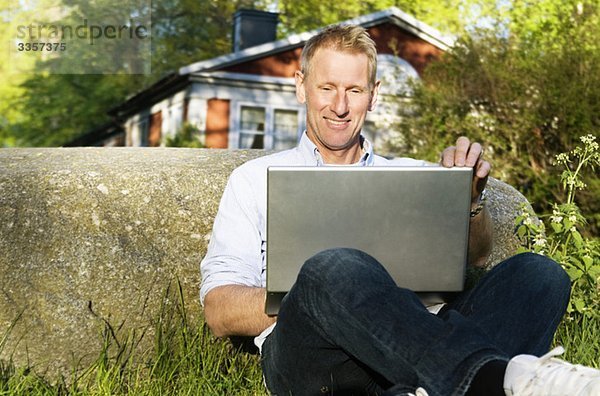 Mann sitzt draußen mit Laptop im Knie