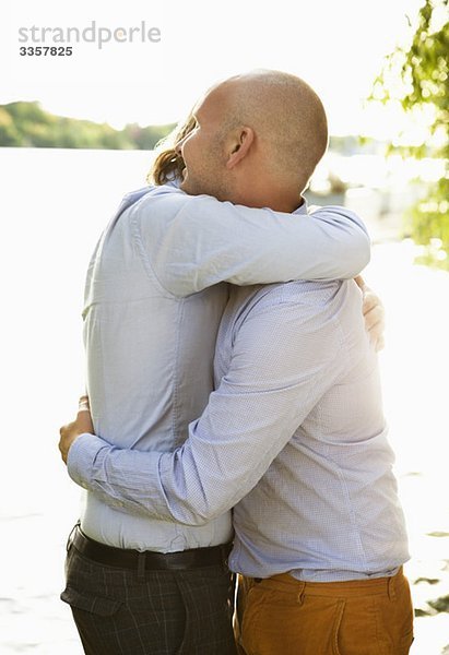 Zwei schwule Männer  die sich am Wasser umarmen.
