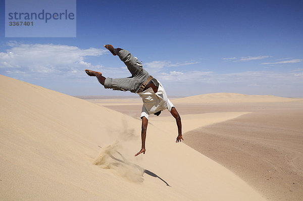 Reiseleiter  Spaß  Skeleton Coast-Nationalpark  in der Nähe von Skeleton Coast Camp  Wilderness Safaris  Region Kunene  Namibia  Afrika  Mann  Salto  Salto  Akrobatik  funny  genießen  Sandy  Sand  Wüste  Natur  Hang  Sprung