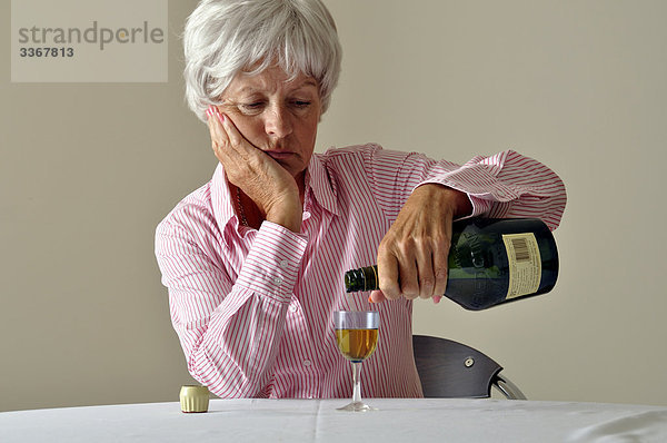 Interior  zu Hause  Senior  Senioren  Frau  Glas  Depression  Krankheit  Traurigkeit  1  reifer Erwachsene  reife Erwachsene  Alkohol  Einsamkeit  trinken  Flasche  Likör  alt  Sherry