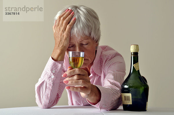 Interior  zu Hause  Senior  Senioren  Frau  Glas  Kopfschmerz  Depression  Krankheit  Traurigkeit  1  Verzweiflung  Alkohol  Einsamkeit  trinken  Flasche  betrunken  Likör  alt