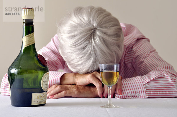 Interior  zu Hause  Senior  Senioren  Frau  Glas  Kopfschmerz  Depression  Krankheit  Traurigkeit  schlafen  1  Verzweiflung  Alkohol  Einsamkeit  trinken  Flasche  betrunken  Likör  alt
