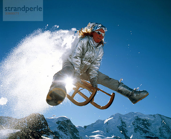 Schweiz  Wintersport  Schlitten  Schlitten  Sprung  Kapern  Berge  Sonne  zurück Licht  Frau  Person  blauer Himmel  Himmel  Pulverschnee