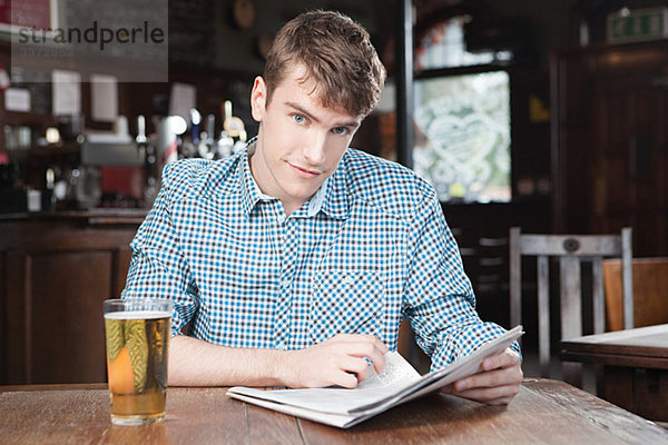 Junger Mann in der Bar mit Zeitung und Bier