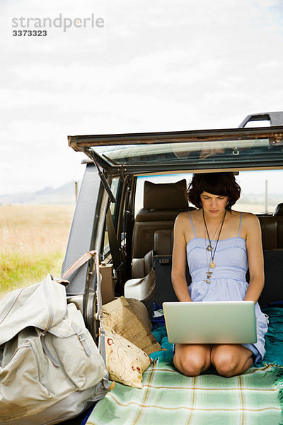 Junge Frau mit Laptop im hinteren Teil des Geländewagens