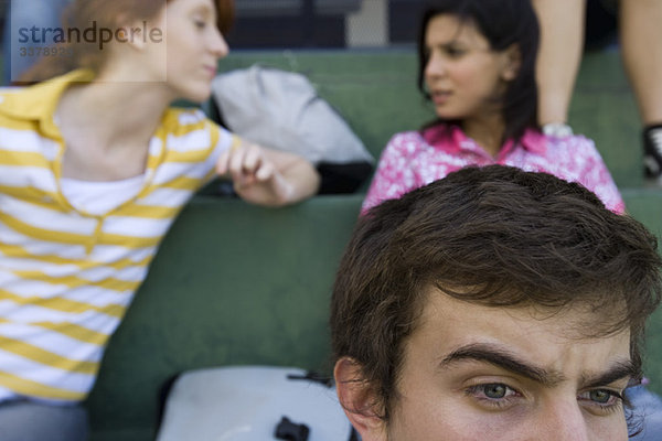 Hohe Schulfreunde sitzen zusammen auf Tribünen  Junge schaut aufmerksam zu  Mädchen im Hintergrund plaudern