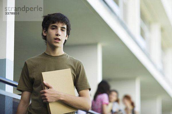 Männlicher Gymnasiast mit Binder unter dem Arm