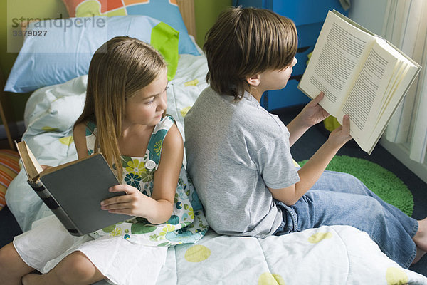 Geschwister lesen zusammen  Mädchen blickt über die Schulter zu Bruder's Buch