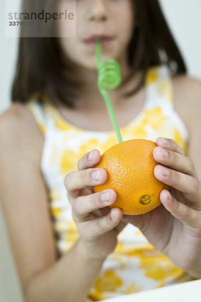 Mädchen trinkt Saft aus Orangenhälfte durch Stroh