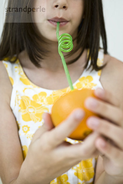 Mädchen trinkt Saft aus Orangenhälfte durch Stroh
