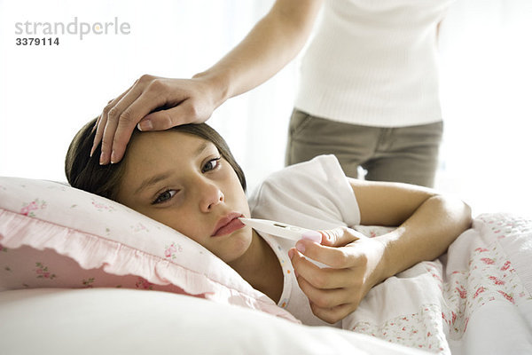 Mädchen bei der Temperaturkontrolle mit Thermometer  Mutter streichelt Stirn