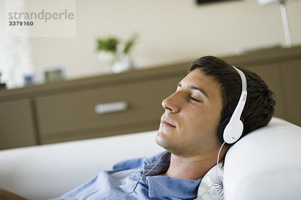 Junger Mann entspannt auf dem Sofa Musik hören mit Kopfhörern