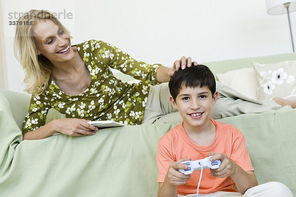 Junge sitzt auf dem Boden und spielt Videospiel  Mutter entspannt auf dem Sofa.