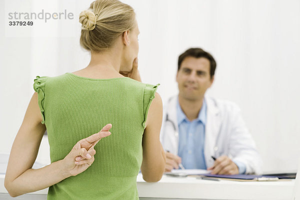 Patientin mit Hand hinter dem Rücken  die die Finger kreuzt und mit dem Arzt spricht.