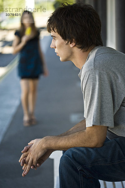 Junger Mann auf Gehsteigbank sitzend
