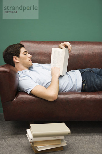 Junger Mann entspannt auf Sofa mit Buch