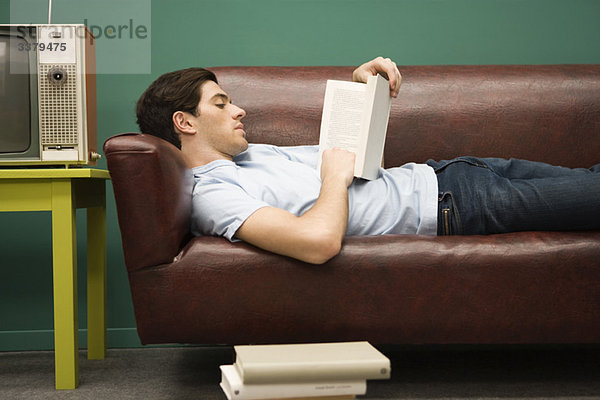 Junger Mann entspannt auf Sofa mit Buch