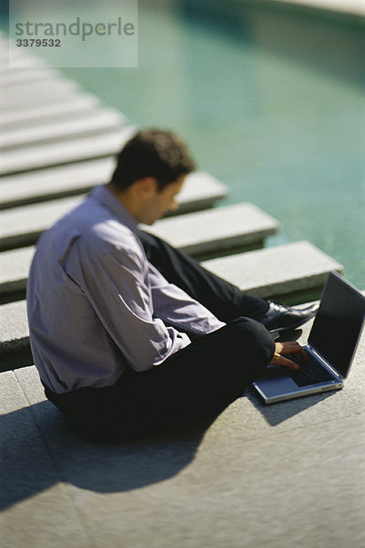 Geschäftsmann auf dem Boden neben dem Pool sitzend  mit Laptop-Computer
