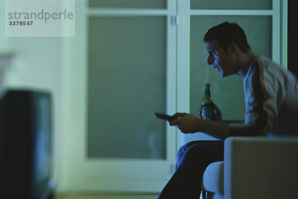 Mann beim Fernsehen  hält Bier und Fernbedienung  Seitenansicht