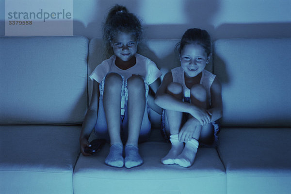 Zwei Mädchen  die nachts zusammen fernsehen  beide lächeln.