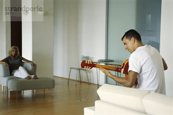 Mann spielt Akustikgitarre im Wohnzimmer  Frau schaut zu