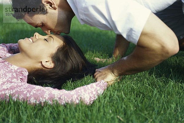 Junges Paar entspannt auf Gras  Mann küsst die Stirn der Frau