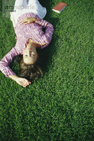 Junge Frau schläft auf Gras  Buch auf dem Boden neben ihr liegend