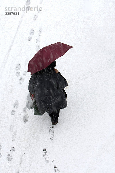Frau mit Regenschirm und Einkaufstüten läuft durch den Schnee  Vogelperspektive