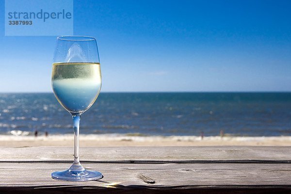 Glas mit Weißwein steht auf Holzbrett  Meer im Hintergrund  Wenningstedt-Braderup  Sylt  Deutschland