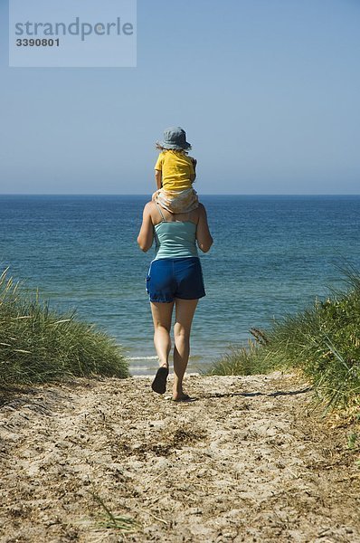Frau zu Fuß in Richtung Meer mit einem Kind auf ihre Schultern  Schweden.