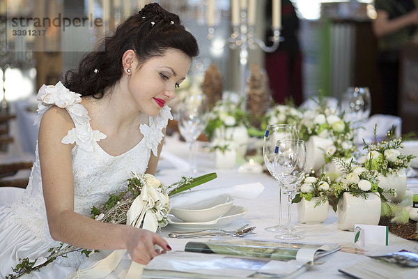 Braut sitzt an einem gedeckten Tisch und liest eine Zeitschrift