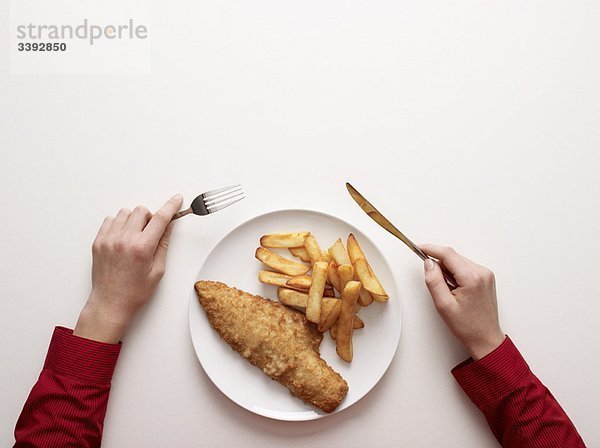 Hände bei einem Teller Fisch und Pommes frites