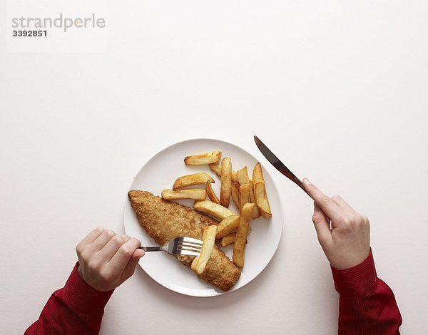 Hände auf dem Teller mit Fisch und Pommes frites