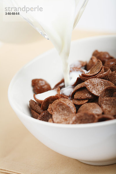 Milch wird in ein Glas mit Cornflakes gegossen  Close-up