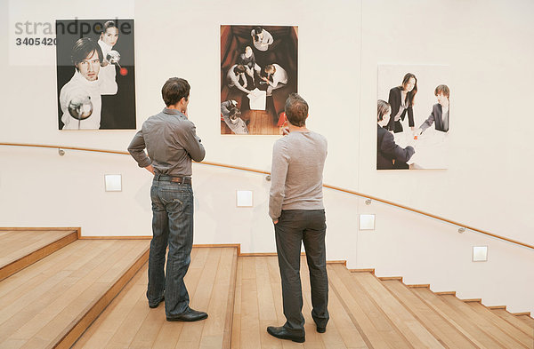 Zwei Männer gucken Fotografien an der Wand an