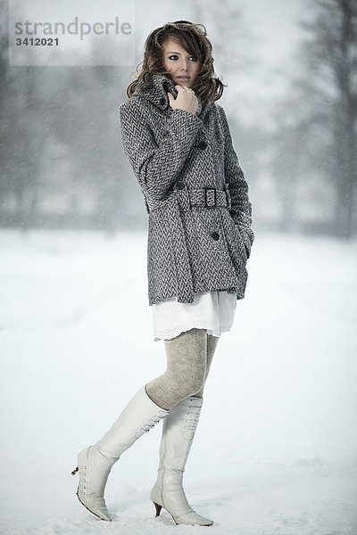 Junge Frau steht mit Poncho im Schnee