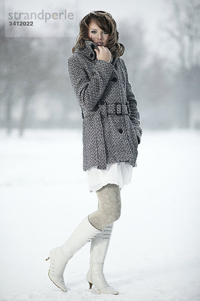 Junge Frau steht mit Poncho im Schnee