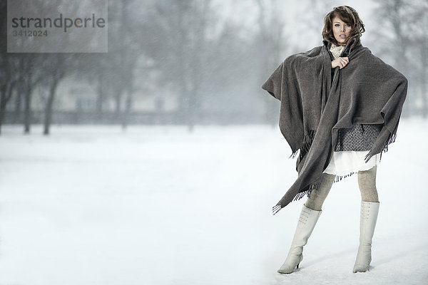 Junge Frau steht mit Poncho im Schnee