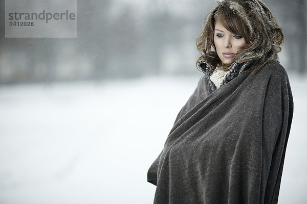 Junge Frau steht mit Poncho im Schnee