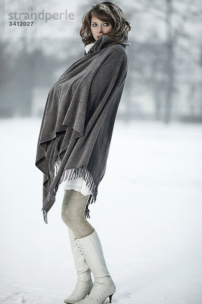 Junge Frau steht mit Poncho im Schnee