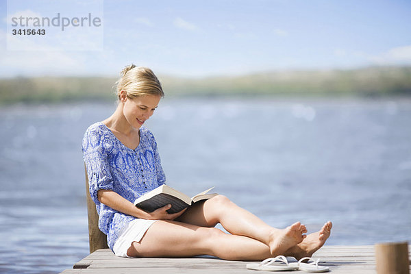 Frau beim Lesen eines Buches am See