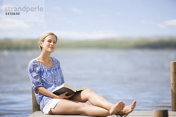 Frau beim Lesen eines Buches am See