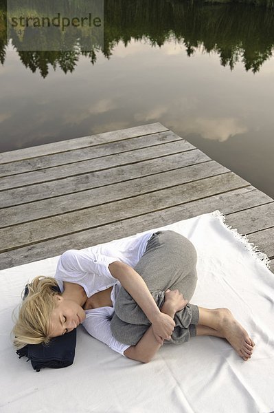 Junge Frau auf Decke am See liegend