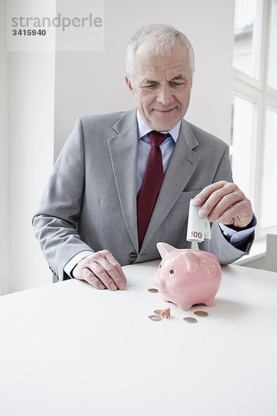 Mann legt Banknote ins Sparschwein