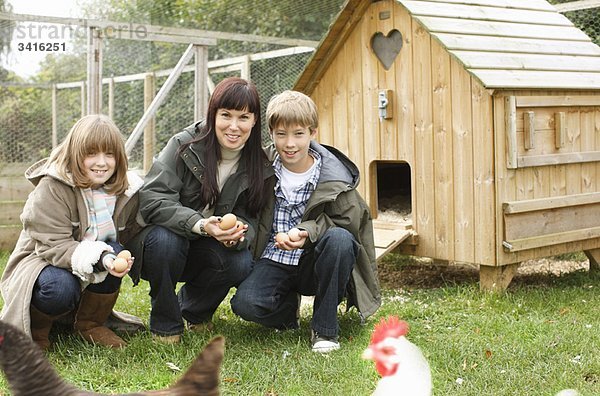 Mutter und Kinder beim Füttern von Hühnern